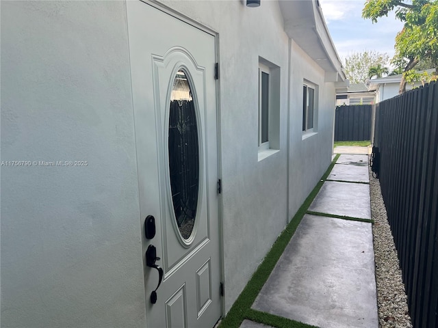 view of exterior entry with fence and stucco siding