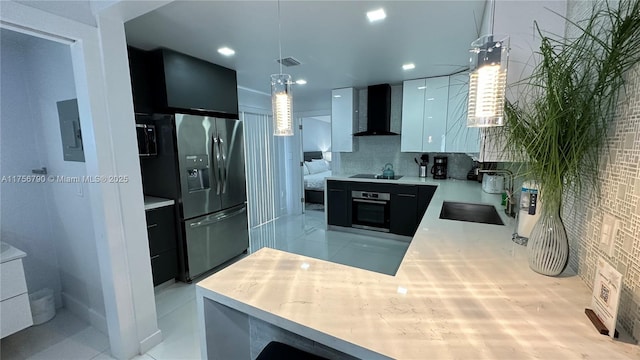 kitchen with visible vents, wall chimney range hood, light countertops, appliances with stainless steel finishes, and a sink