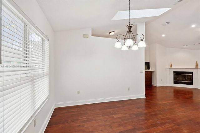 interior space featuring visible vents, wood finished floors, a glass covered fireplace, vaulted ceiling with skylight, and baseboards