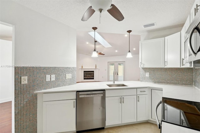 kitchen with visible vents, a peninsula, white cabinets, stainless steel appliances, and a sink