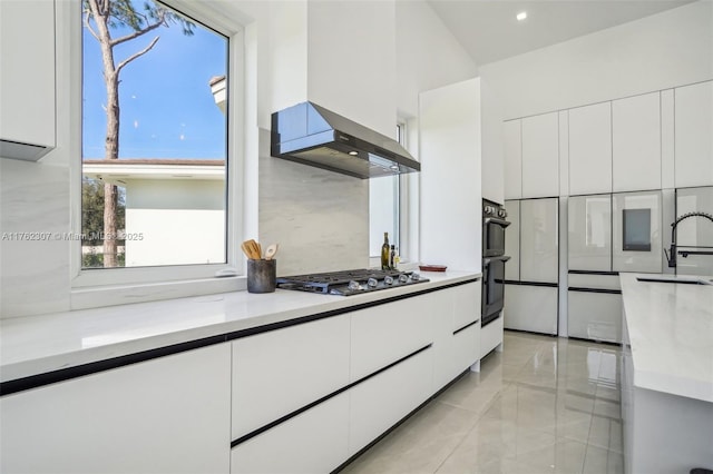 kitchen with modern cabinets, dobule oven black, white cabinetry, wall chimney range hood, and stainless steel gas cooktop