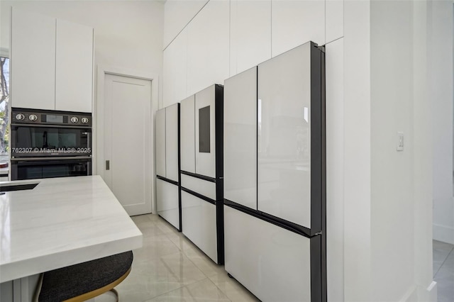 kitchen with fridge, light stone countertops, white cabinets, and dobule oven black