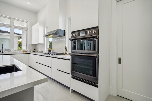 kitchen featuring light countertops, white cabinets, dobule oven black, wall chimney range hood, and modern cabinets