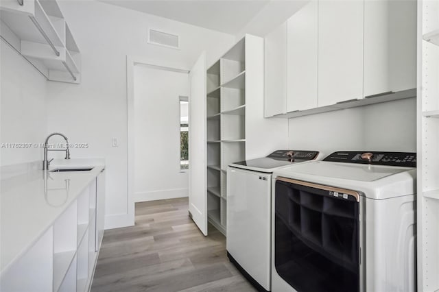 laundry area featuring visible vents, light wood-style flooring, cabinet space, independent washer and dryer, and a sink