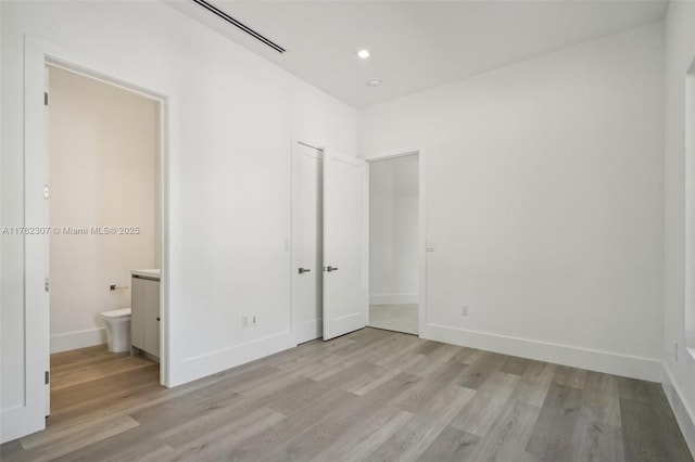 unfurnished bedroom with connected bathroom, baseboards, and light wood-style flooring