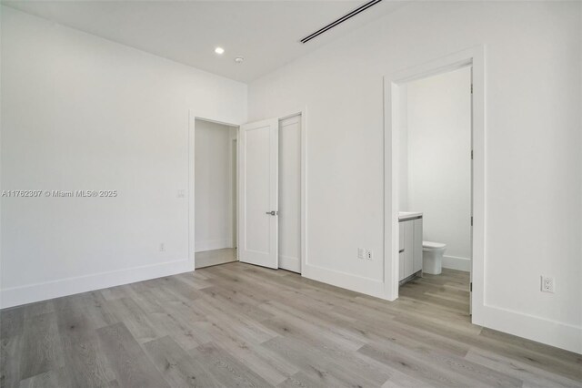 unfurnished bedroom with recessed lighting, baseboards, wood finished floors, and ensuite bathroom