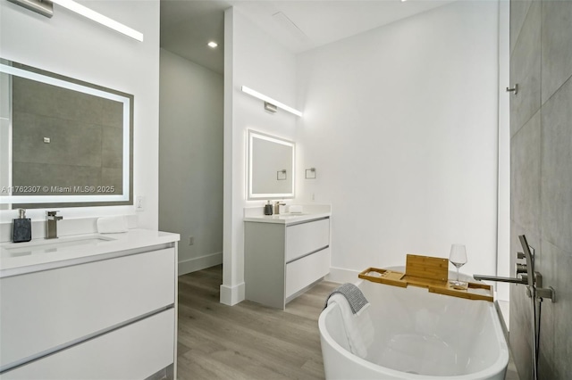 full bath featuring baseboards, a freestanding bath, two vanities, wood finished floors, and a sink