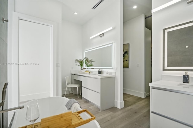 full bathroom featuring wood finished floors, visible vents, two vanities, recessed lighting, and a freestanding bath