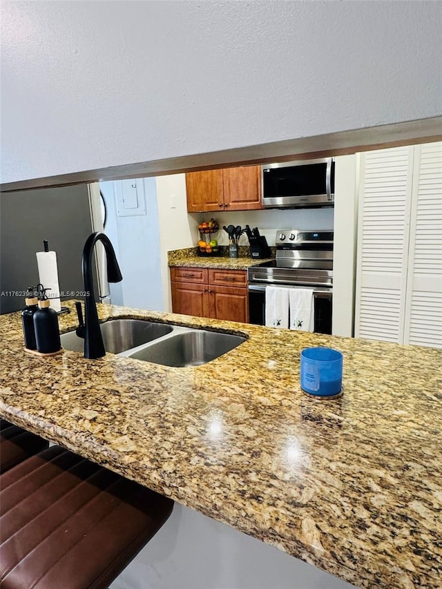 kitchen with a sink, stainless steel appliances, light stone counters, and brown cabinetry