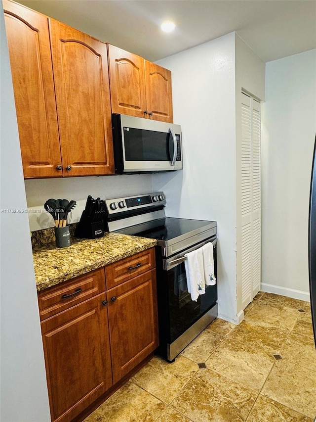 kitchen with brown cabinets, light stone countertops, baseboards, and stainless steel appliances