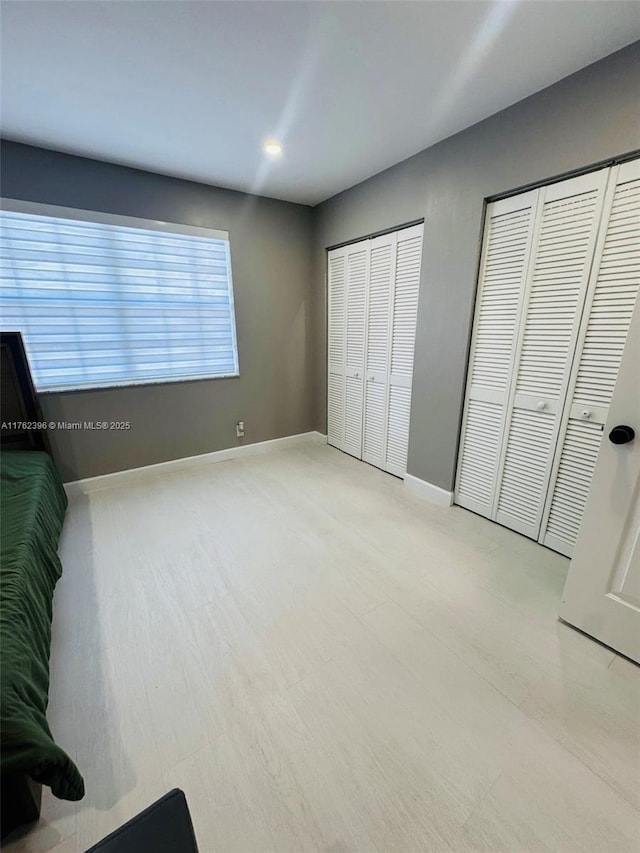 unfurnished bedroom featuring baseboards, two closets, and wood finished floors