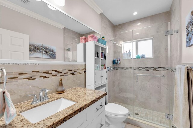 bathroom with crown molding, toilet, vanity, a stall shower, and tile walls