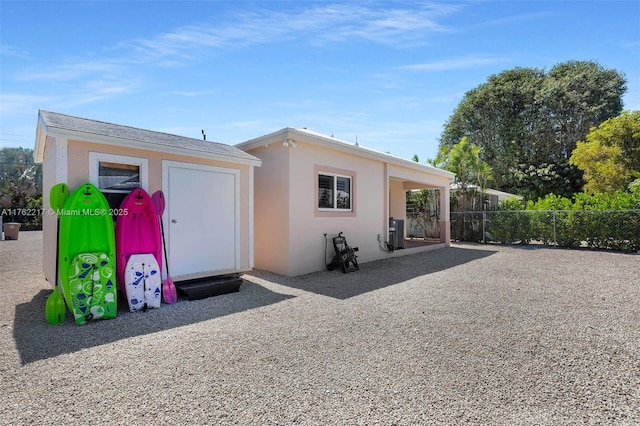 view of front of property with an outdoor structure, central air condition unit, fence, and stucco siding