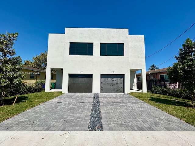 modern home with stucco siding, an attached garage, decorative driveway, and a front lawn