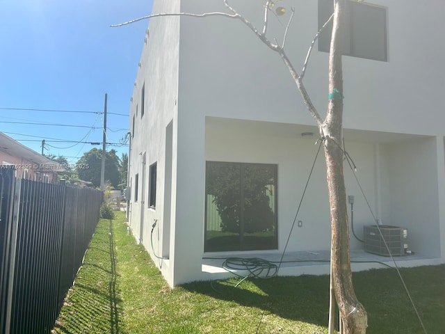 view of home's exterior with stucco siding, a lawn, cooling unit, and fence