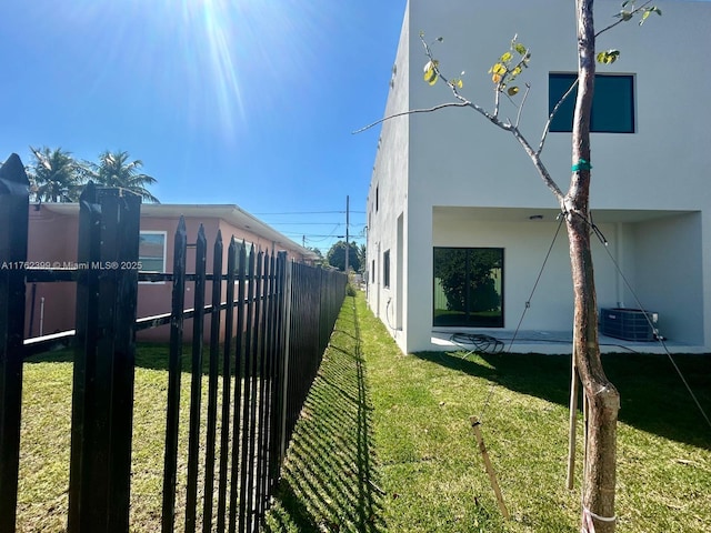 view of side of property featuring central AC unit, stucco siding, a lawn, and fence