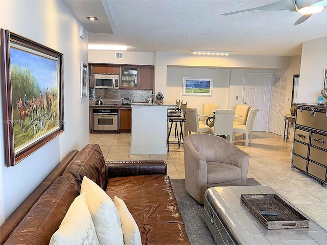 living area with light tile patterned floors, visible vents, a textured ceiling, and a ceiling fan