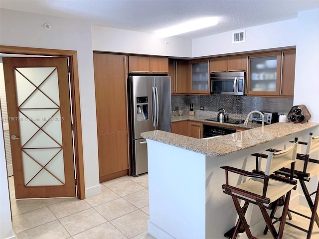 kitchen with visible vents, light stone counters, appliances with stainless steel finishes, a breakfast bar area, and a peninsula