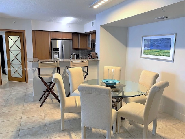 dining area with light tile patterned flooring, visible vents, a textured ceiling, and baseboards