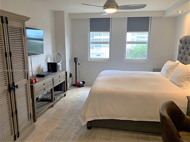 bedroom featuring light tile patterned flooring, a ceiling fan, and a textured ceiling