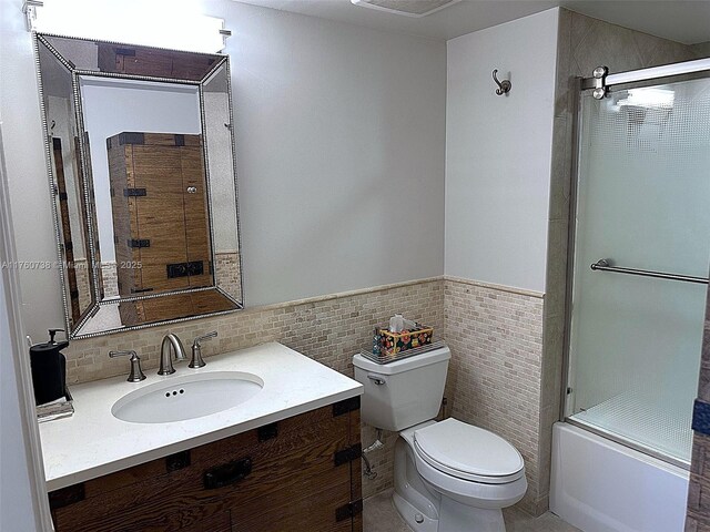 full bath featuring a wainscoted wall, toilet, combined bath / shower with glass door, tile walls, and vanity