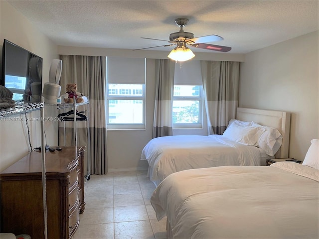 bedroom featuring light tile patterned floors, baseboards, a textured ceiling, and a ceiling fan