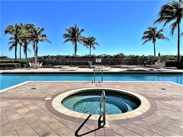 community pool with a patio, fence, and a hot tub