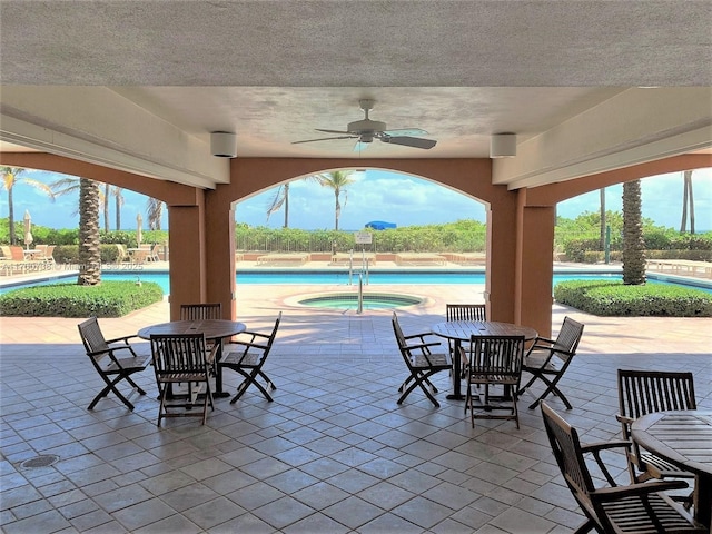 view of patio featuring outdoor dining space, a hot tub, ceiling fan, and a community pool