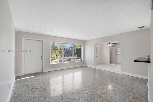 unfurnished room featuring baseboards, speckled floor, arched walkways, and visible vents