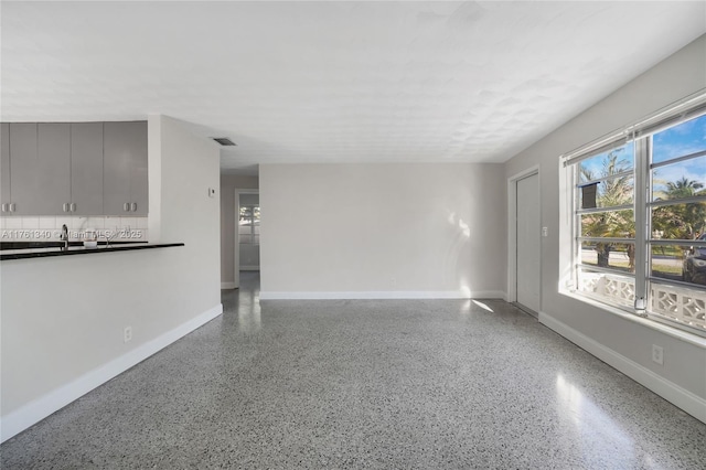 unfurnished living room with visible vents, speckled floor, baseboards, and a sink