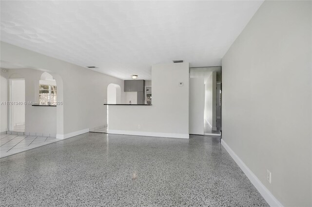 unfurnished living room featuring baseboards, visible vents, speckled floor, and arched walkways