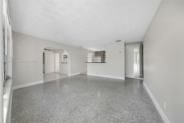 unfurnished living room with speckled floor, visible vents, arched walkways, and baseboards