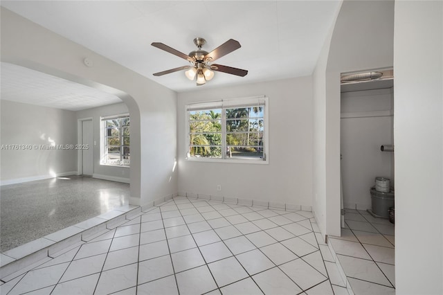 empty room with arched walkways, ceiling fan, baseboards, and light tile patterned flooring