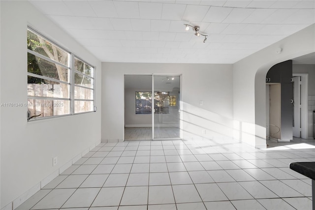 unfurnished room featuring light tile patterned floors, baseboards, and arched walkways