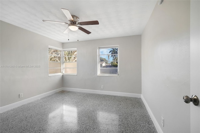 empty room featuring ceiling fan, speckled floor, and baseboards