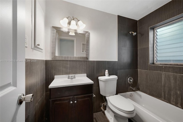 bathroom featuring vanity, a wainscoted wall, tub / shower combination, tile walls, and toilet