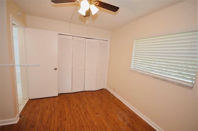 unfurnished bedroom with ceiling fan, baseboards, wood finished floors, a closet, and a textured ceiling