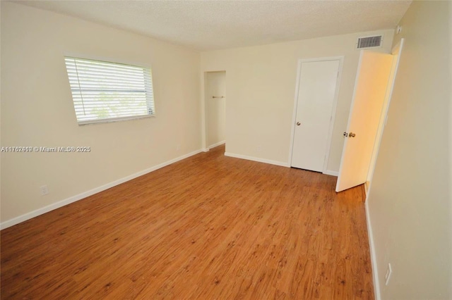 empty room with baseboards, visible vents, a textured ceiling, and light wood-style floors