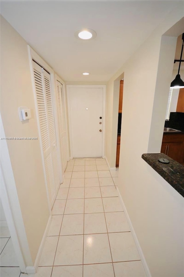 hall featuring light tile patterned floors, baseboards, and a sink