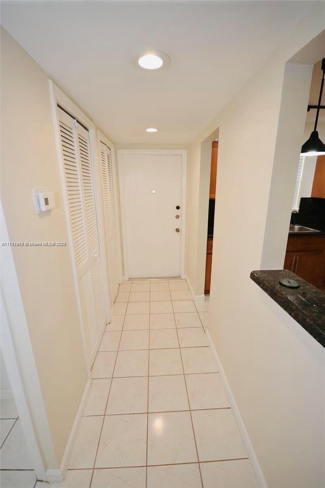 corridor with light tile patterned floors, recessed lighting, baseboards, and a sink