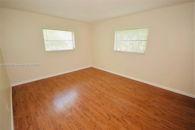 empty room featuring a wealth of natural light, baseboards, and wood finished floors