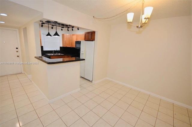 kitchen with dark countertops, baseboards, light tile patterned floors, a peninsula, and white refrigerator with ice dispenser