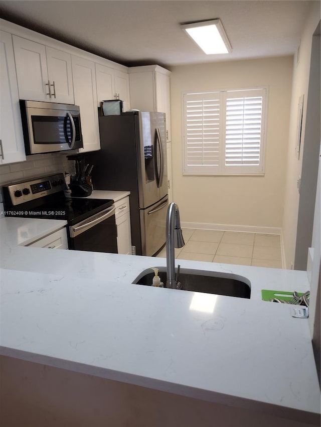 kitchen with a sink, stainless steel appliances, white cabinets, tile patterned floors, and tasteful backsplash