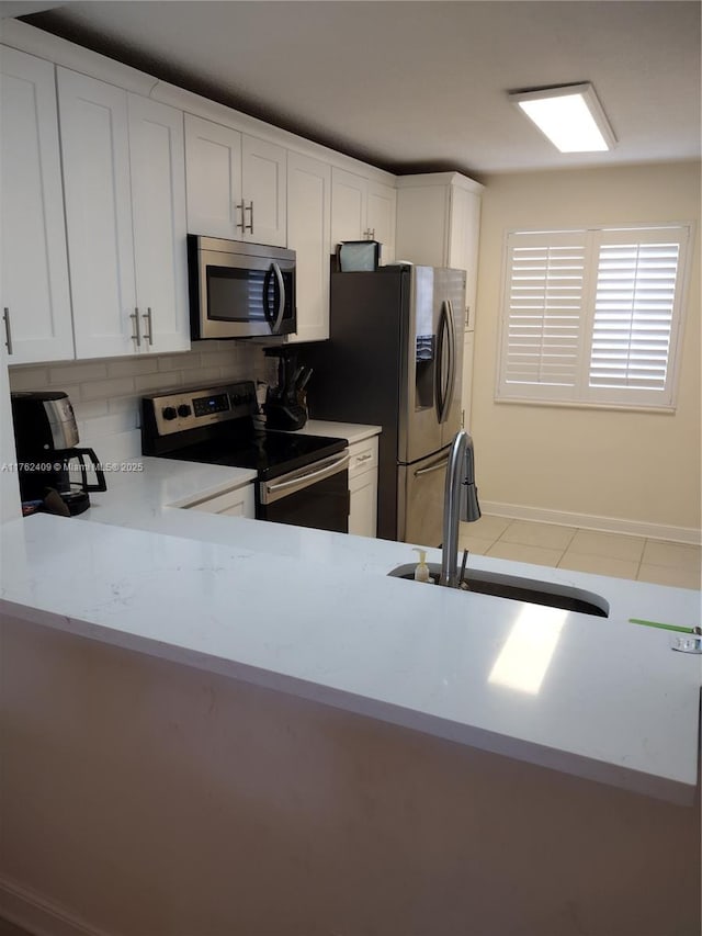 kitchen with tile patterned flooring, tasteful backsplash, stainless steel appliances, white cabinetry, and a sink