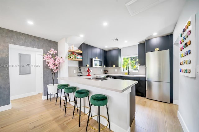 kitchen with a breakfast bar, open shelves, a sink, appliances with stainless steel finishes, and light countertops