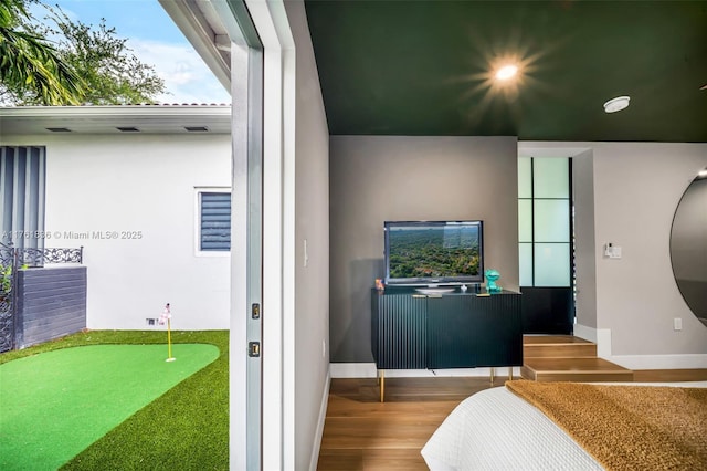 bedroom featuring baseboards, golf simulator, and wood finished floors