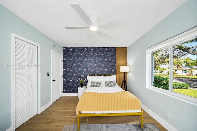 bedroom with visible vents, wood finished floors, wallpapered walls, baseboards, and an accent wall