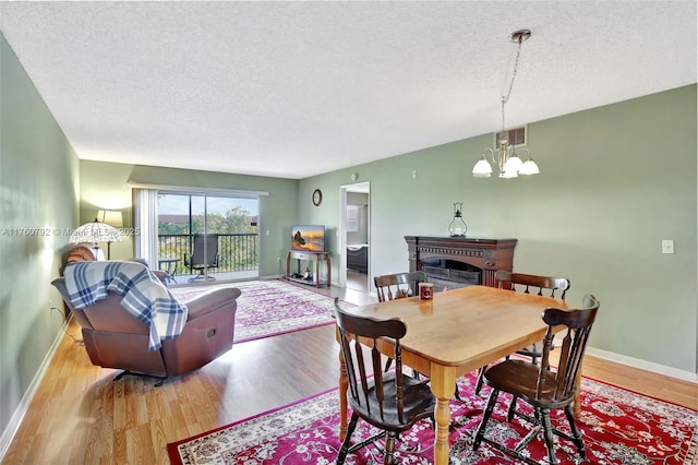 dining room with a notable chandelier, wood finished floors, a fireplace, and a textured ceiling