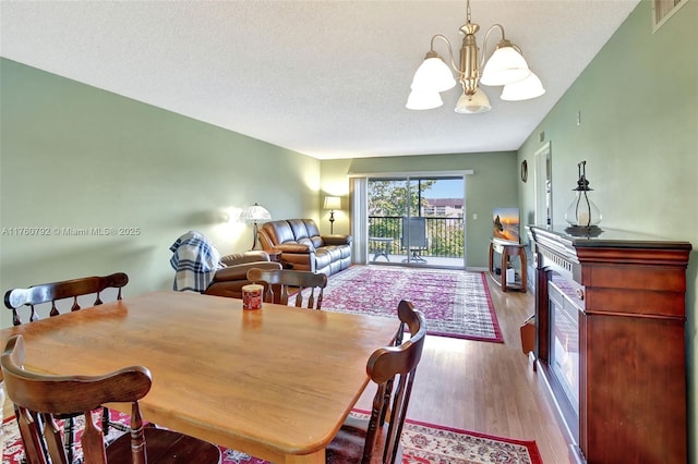 dining area with visible vents, a textured ceiling, wood finished floors, an inviting chandelier, and a fireplace