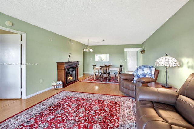 living area with wood finished floors, baseboards, an inviting chandelier, a textured ceiling, and a glass covered fireplace